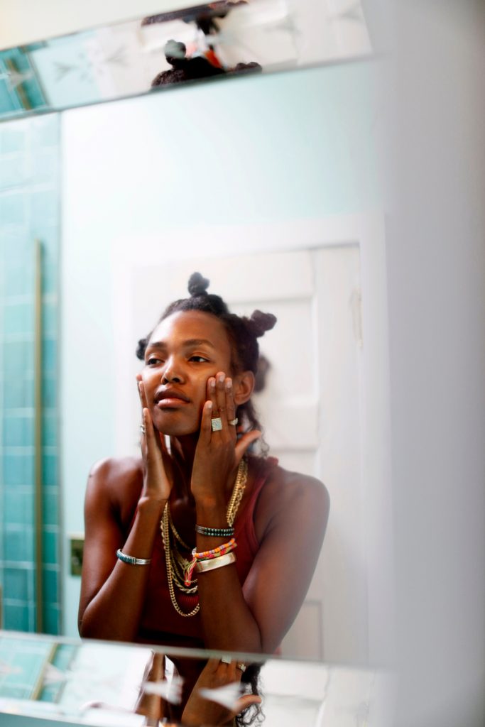 Black woman applying skin care in the mirror.
