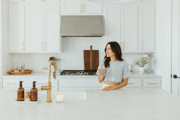 Woman drinking matcha in white kitchen.