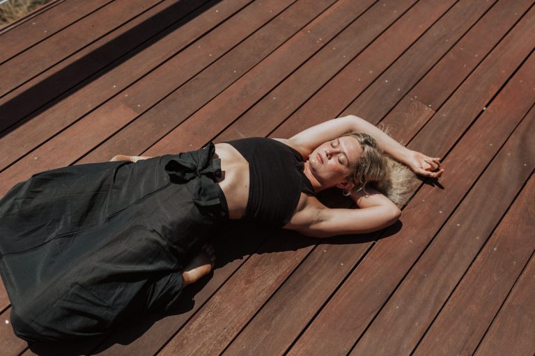 Woman lying with arms outstretched in the sun wearing a black yoga top and skirt 