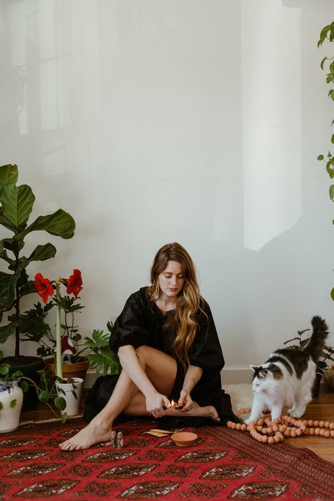 Woman lighting incense sitting on floor next to a cat.