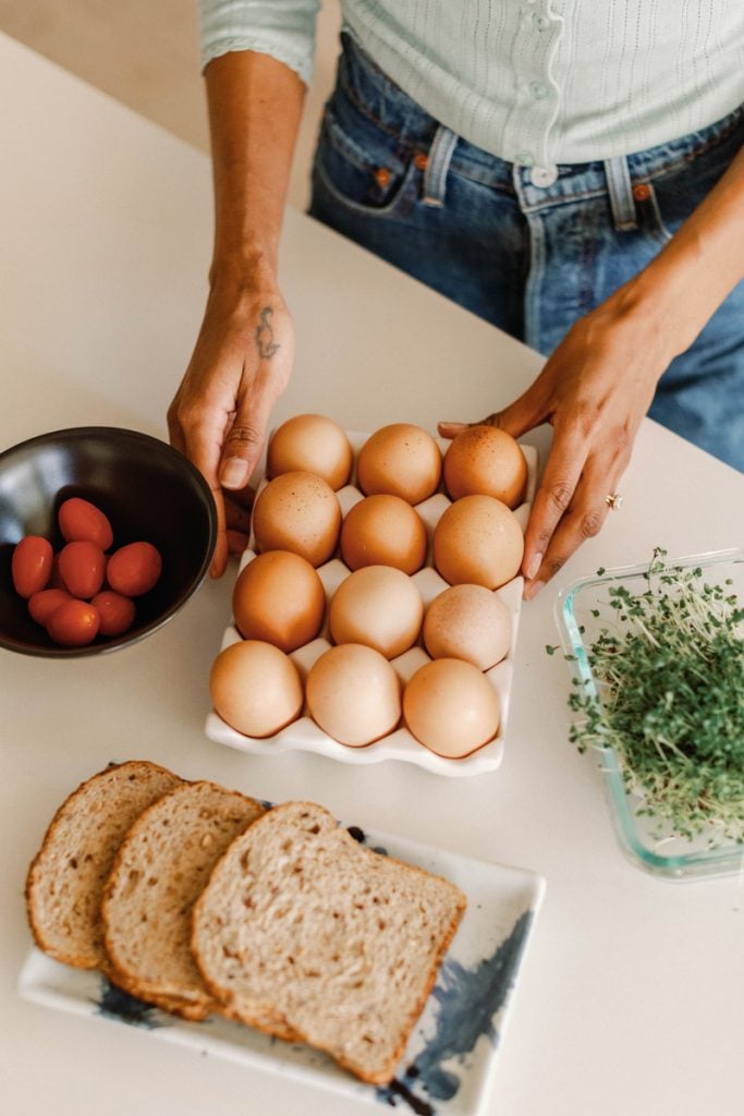 Woman making breakfast with bread, eggs, and tomatoes.