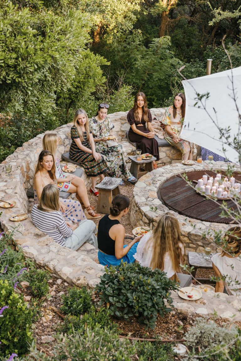 Group of women gathered around outdoor fireplace.