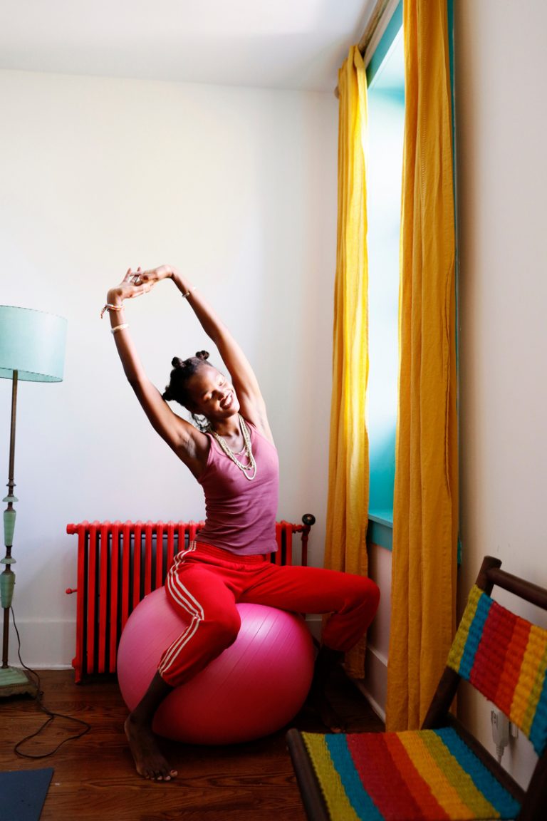 Woman stretching on pink yoga ball by sunny open window