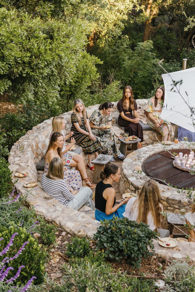 A group of women gathered outside eating around fire pit.