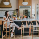 Woman sitting at kitchen island counter drinking coffee.