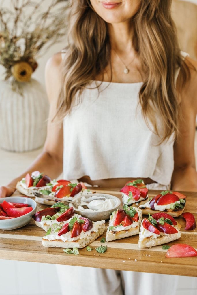 camille styles holding ricotta and plum bruschetta on serving board