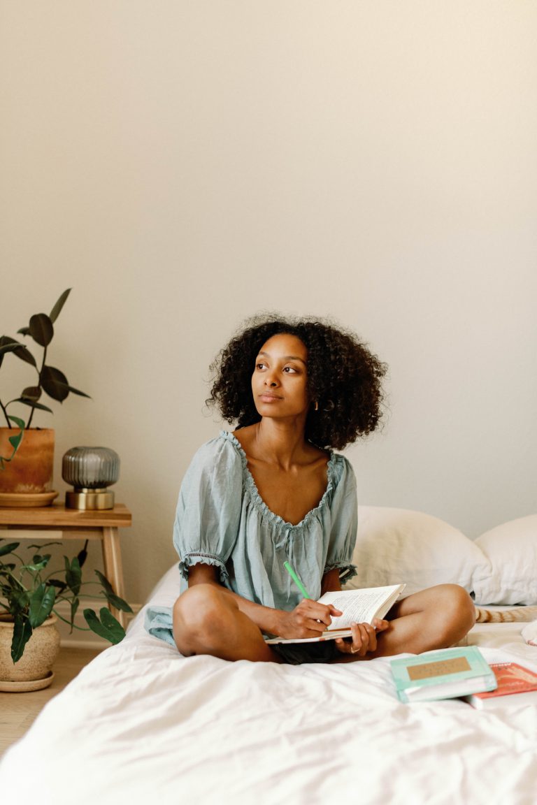 woman sitting on bed writing in journal