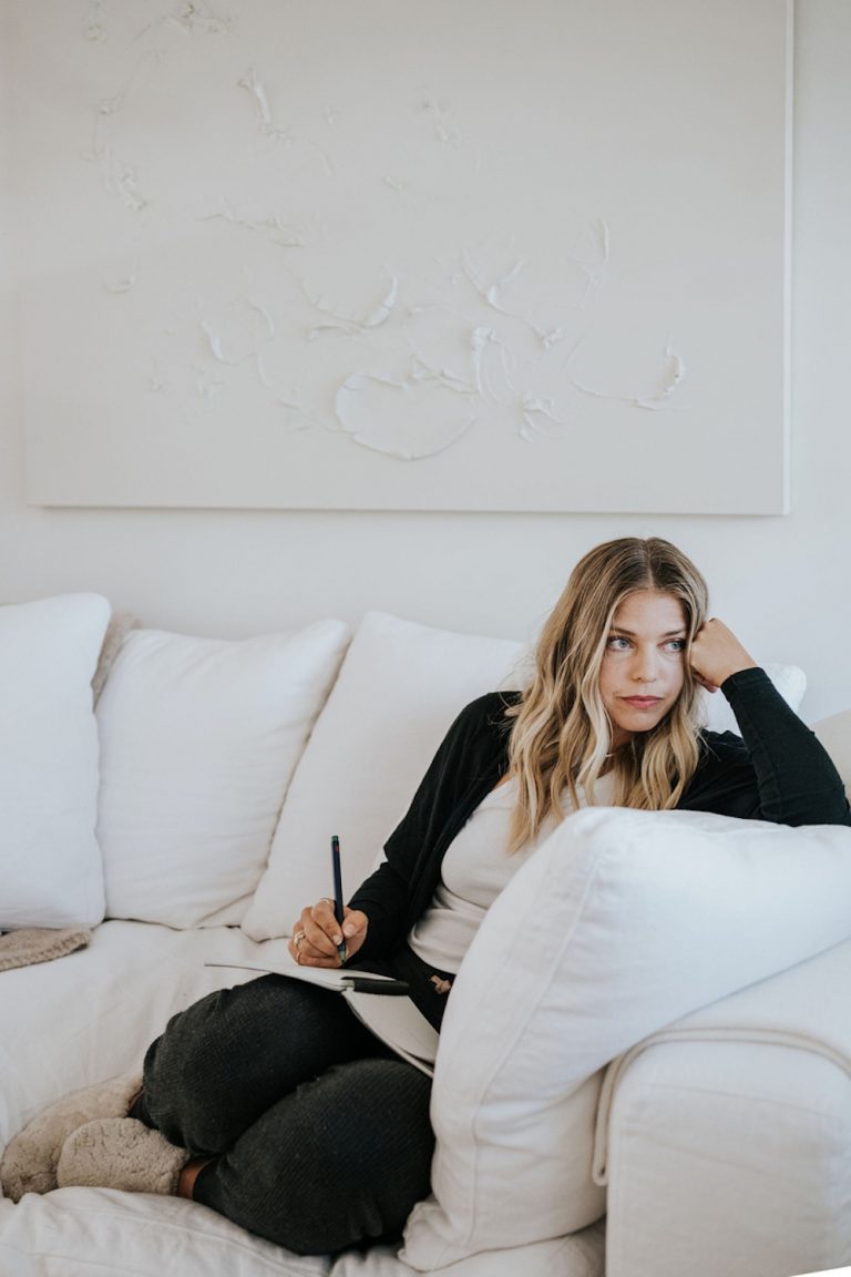 Blonde woman journaling on couch.