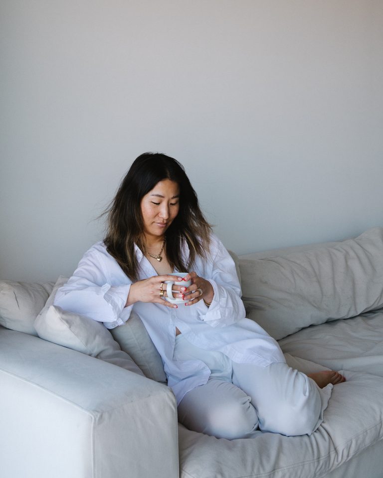 Jennie Yoon sitting on couch drinking coffee.