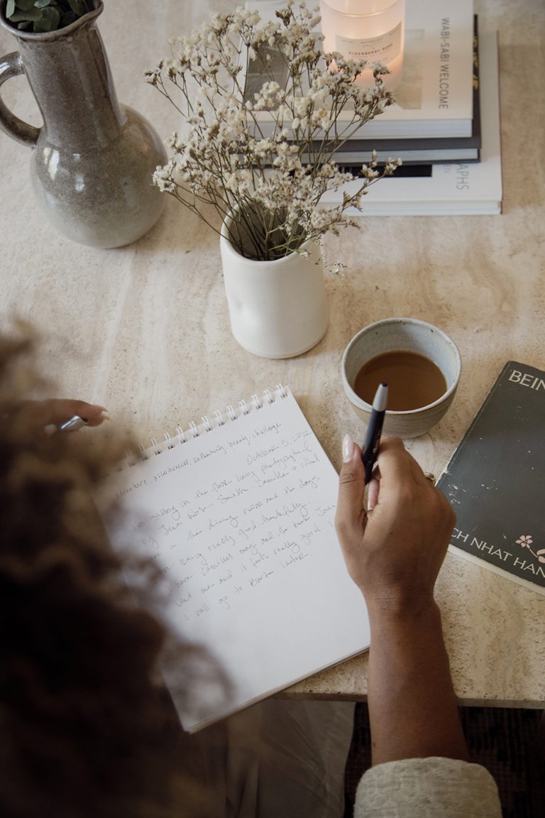 Woman journaling at desk with flowers and coffee.