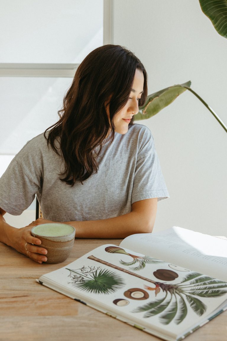 Brunette woman drinking matcha looking at book.