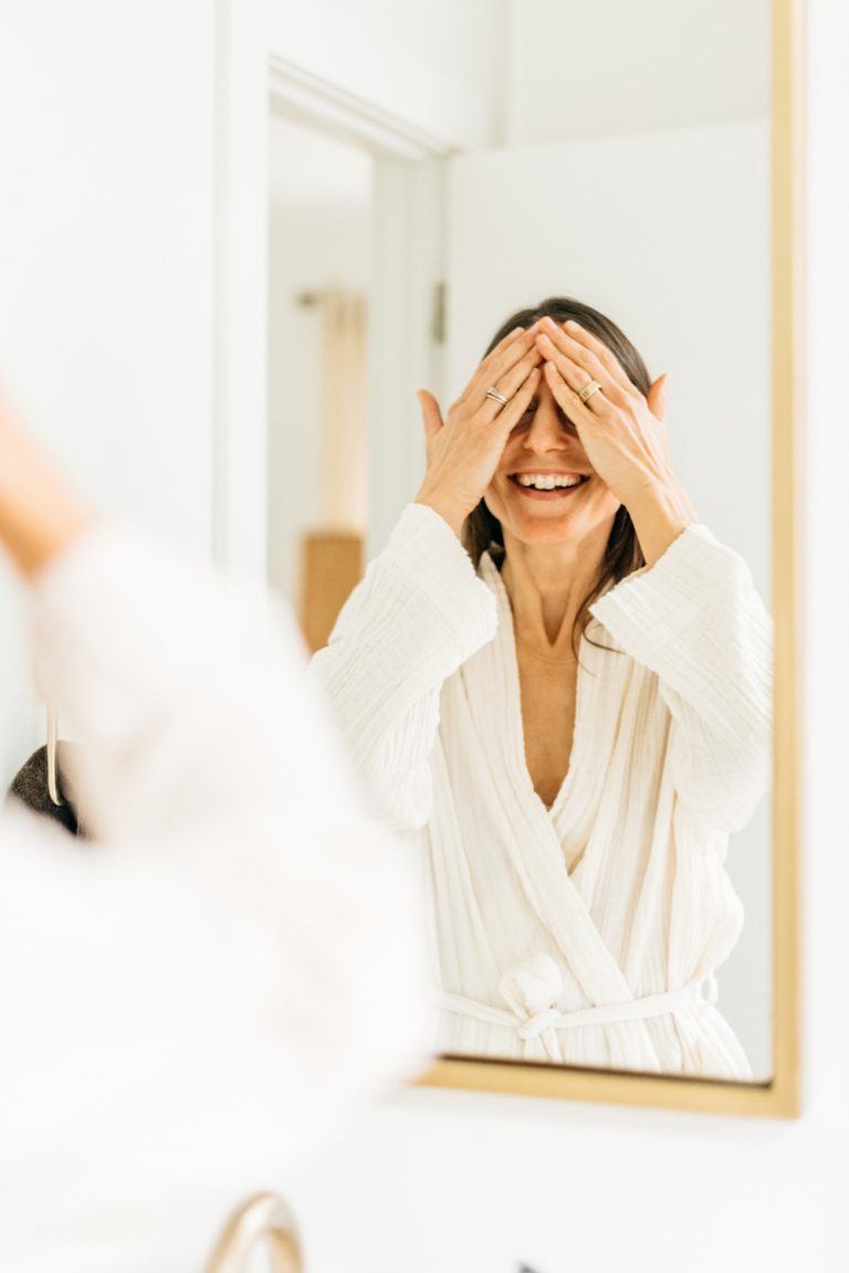 Brunette woman applying skincare in bathroom mirror.