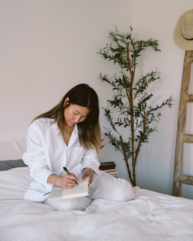 woman writing a list in her journal on a white bed