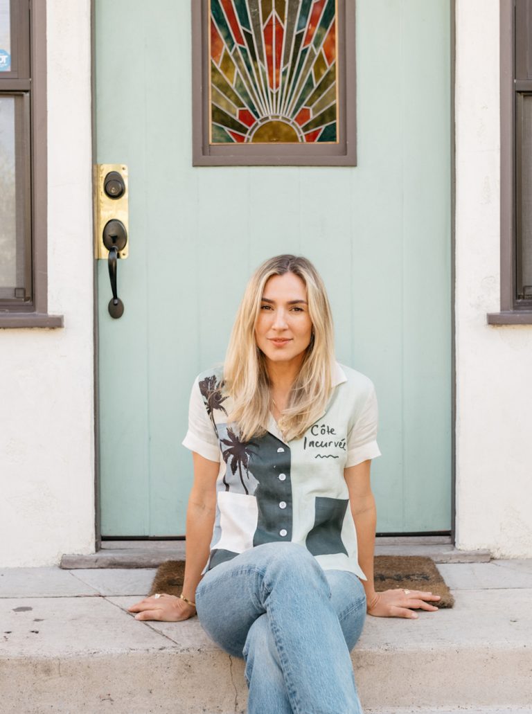 A blonde woman sitting on the doorstep.