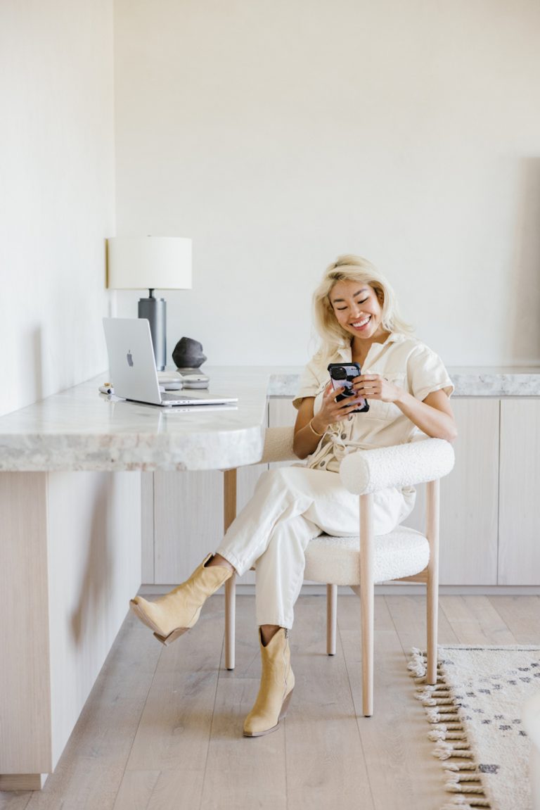 Blonde woman sitting at desk using cell phone.