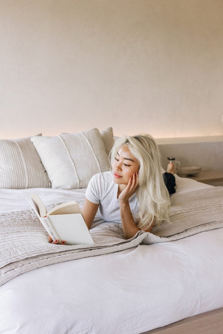 A blonde woman is reading a book in bed.