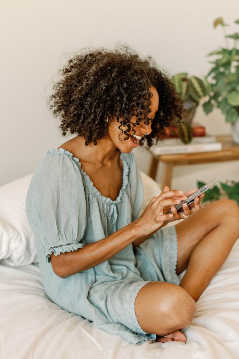 Woman wearing blue nightgown using phone in bed.