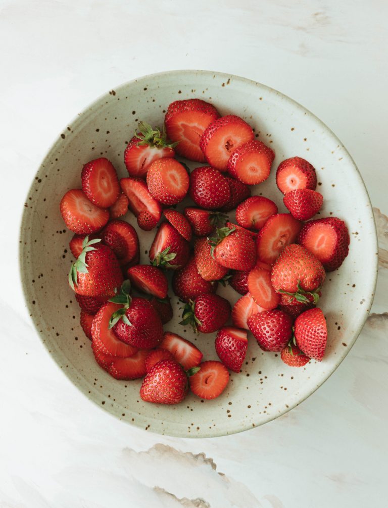 Fresh sliced strawberries in speckled stoneware bowl.
