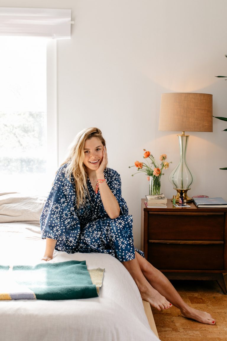 Blonde woman sitting on bed wearing robe.