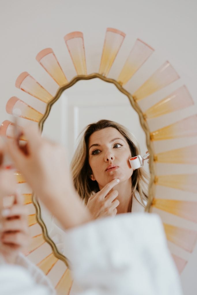 A blonde woman's face is reflected in the mirror.