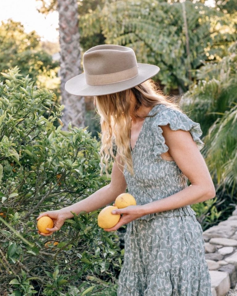 A woman wearing a sun hat is picking lemons outside.