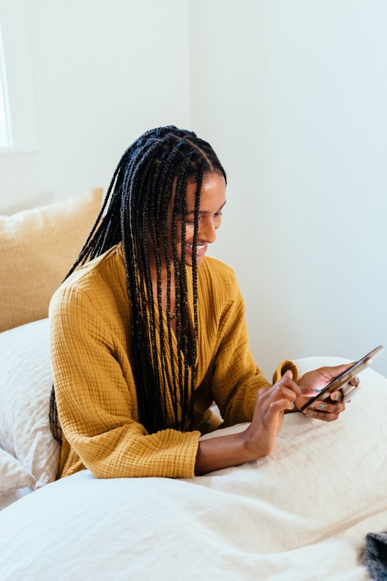 Mujer con bata usando el teléfono en la cama.