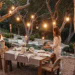 String lights hung from trees outdoors over dining table.