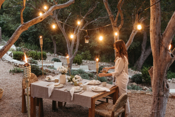 String lights hung from trees outdoors over dining table.