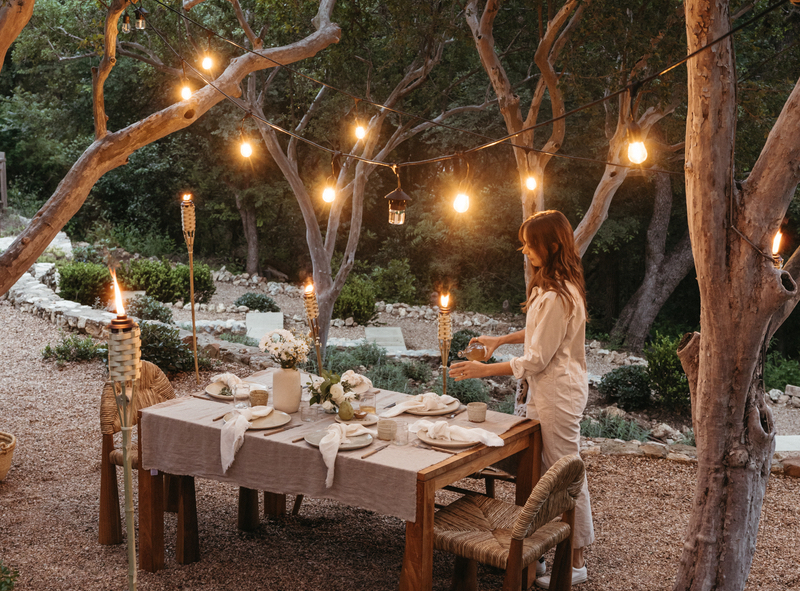 String lights hung from trees outdoors over dining table.