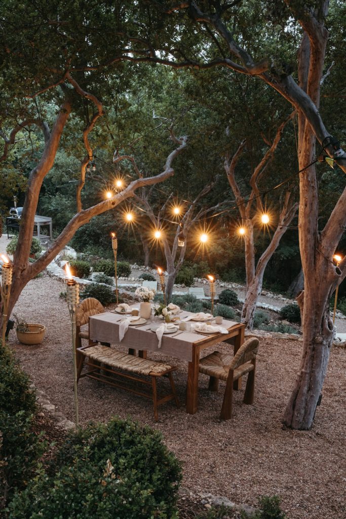 Best string lights strung from trees above outdoor dining table.