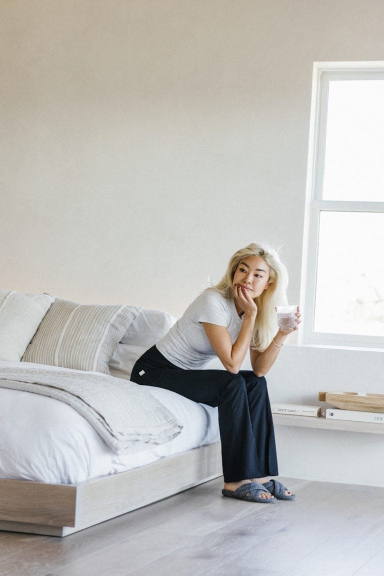 Woman drinking a glass of water sitting on a bed.
