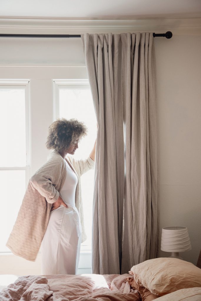 Woman opening curtains in bedroom.