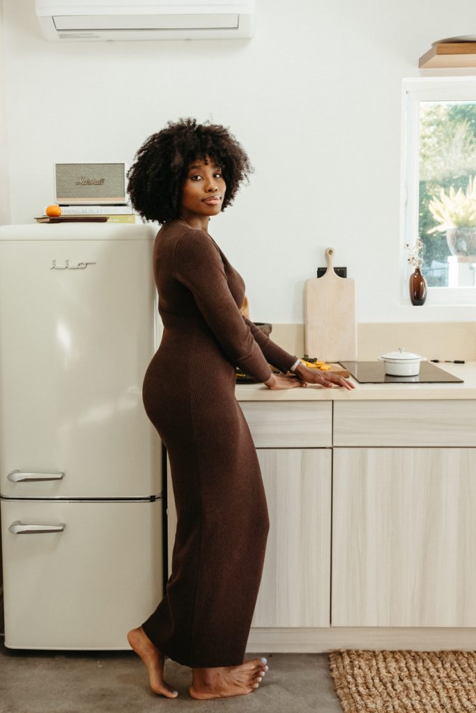 Woman wearing long brown sweater dress standing in kitchen.