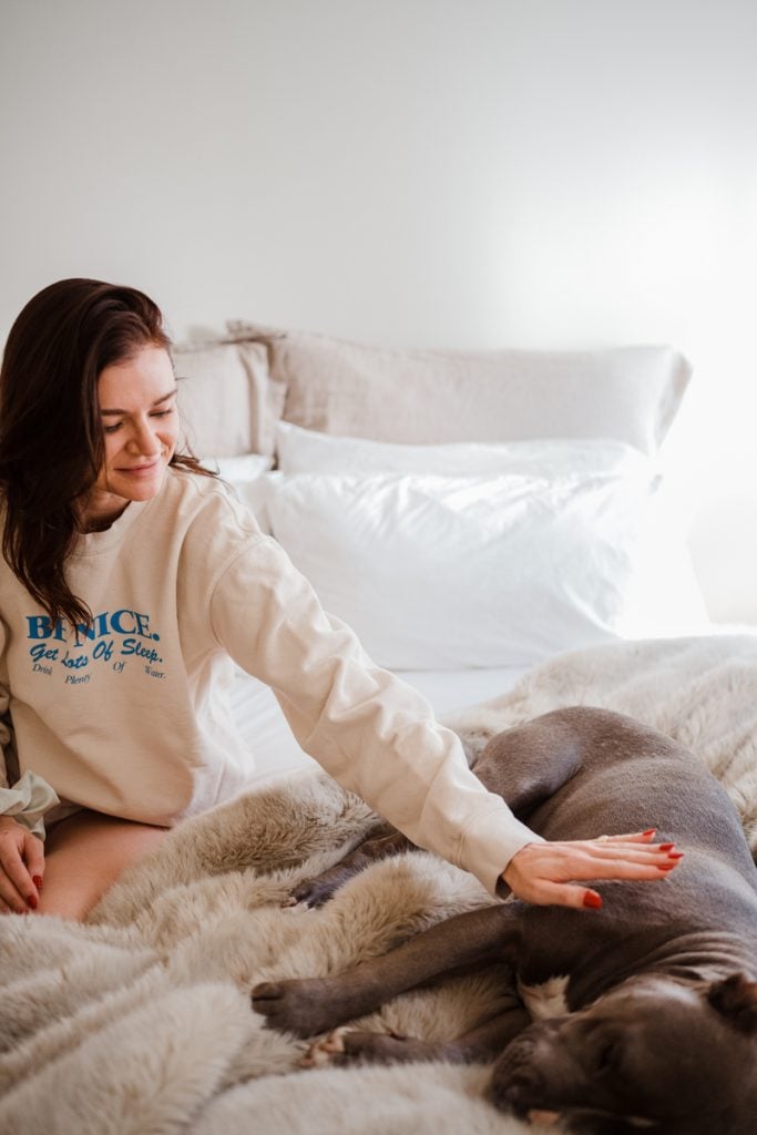 Woman petting dog on bed.