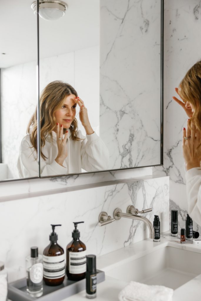 Woman applying skincare in mirror.