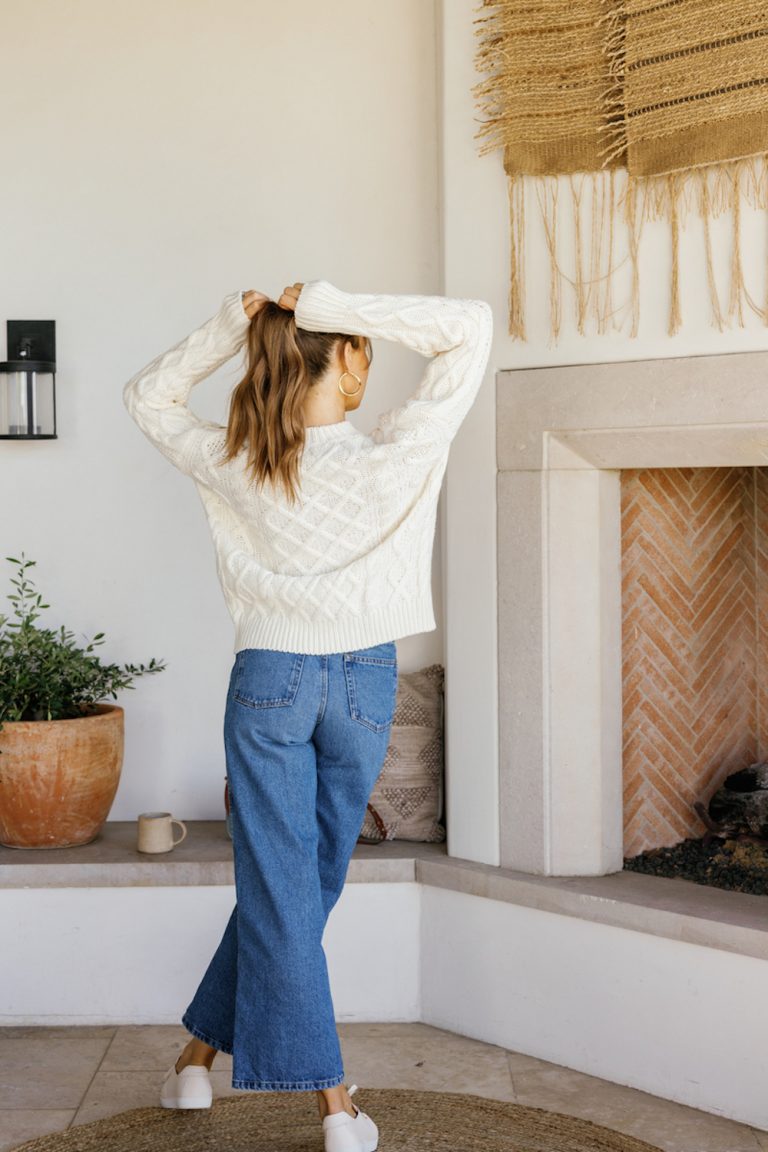 Woman wearing flare denim and white sweater.