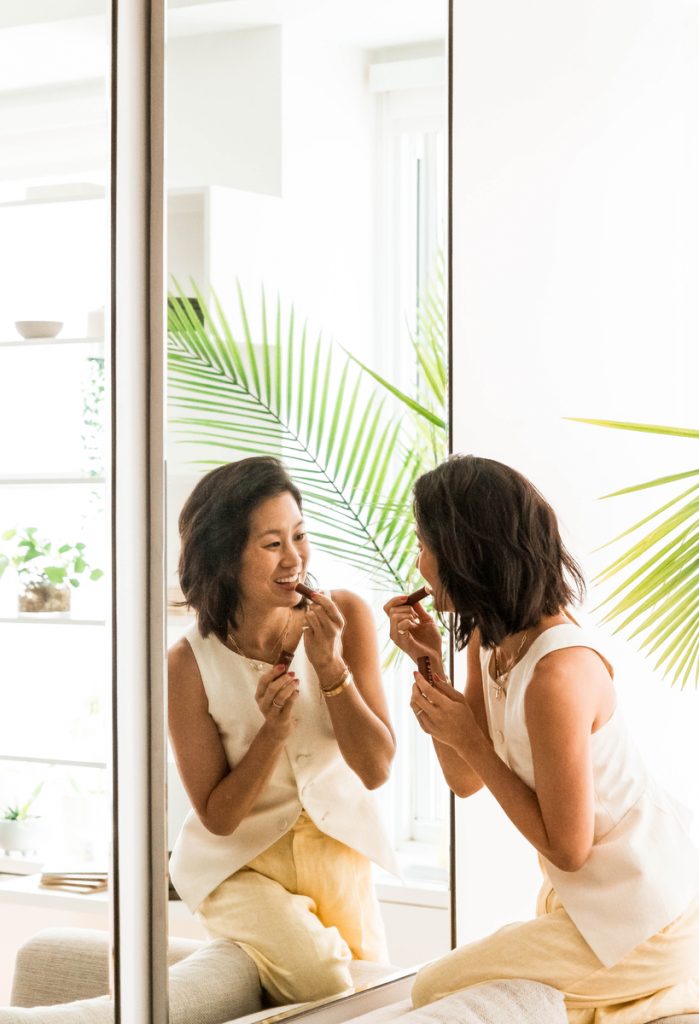 Woman applying lipstick in mirror.