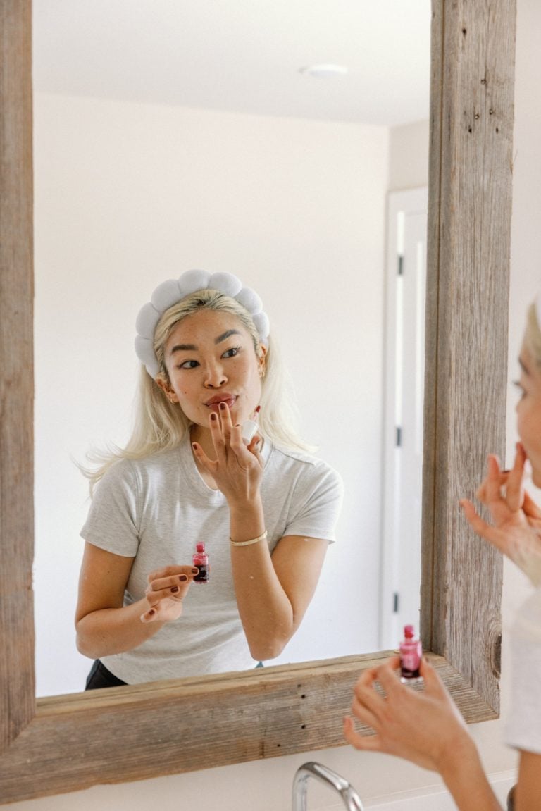 Woman applying lipstick in mirror.