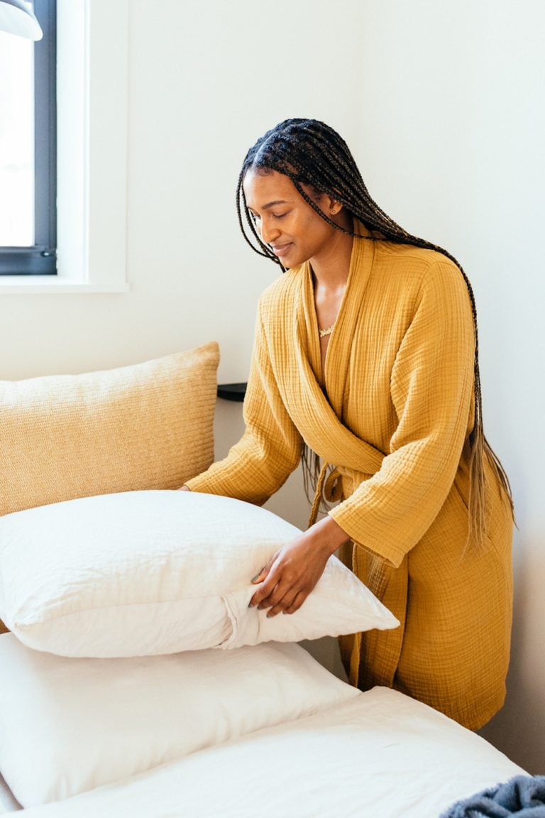 Woman wearing yellow robe making bed.