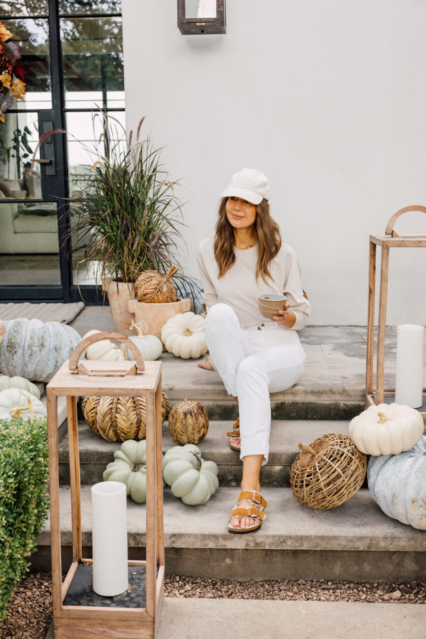 Camille Styles sentada en un porche decorado con calabazas.