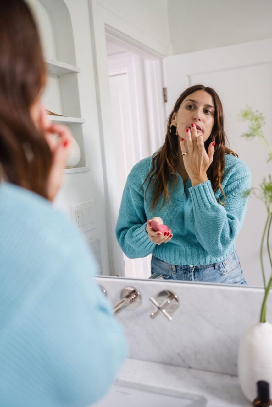 Woman applying lip stain in mirror.