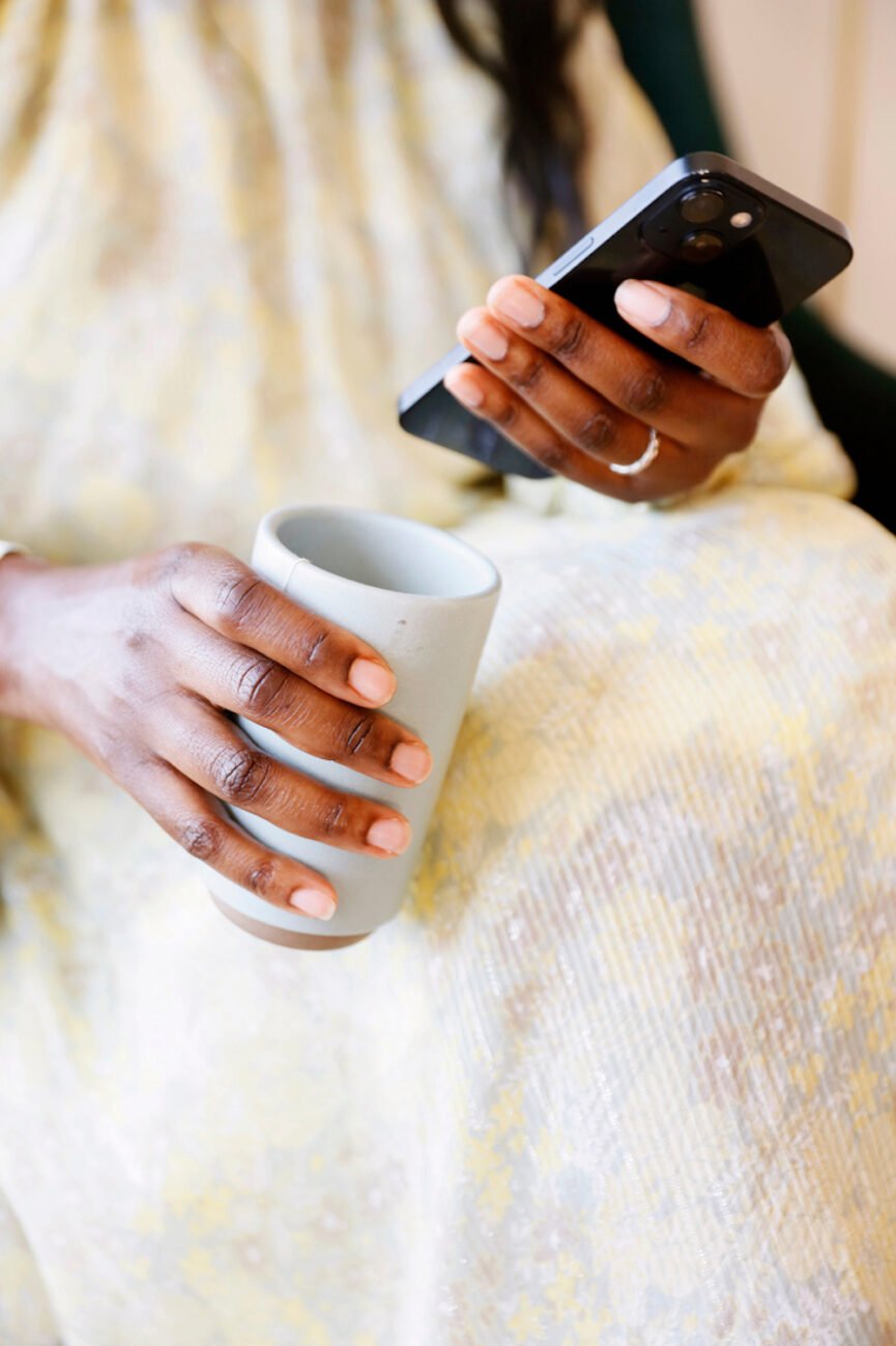 Woman holding cell phone and coffee mug.
