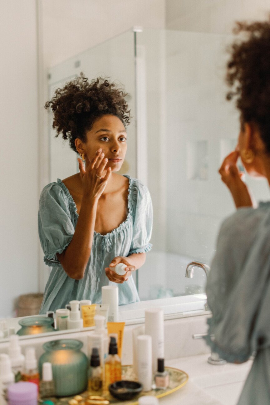 Mujer aplicándose productos para el cuidado de la piel en el espejo.