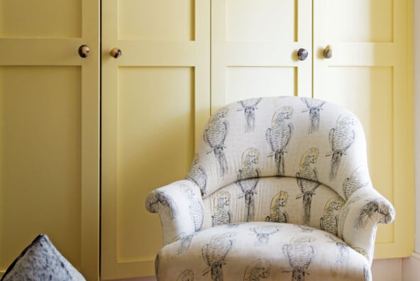 A parrot printed white chair rests on a red rug in front of pale yellow closet doors