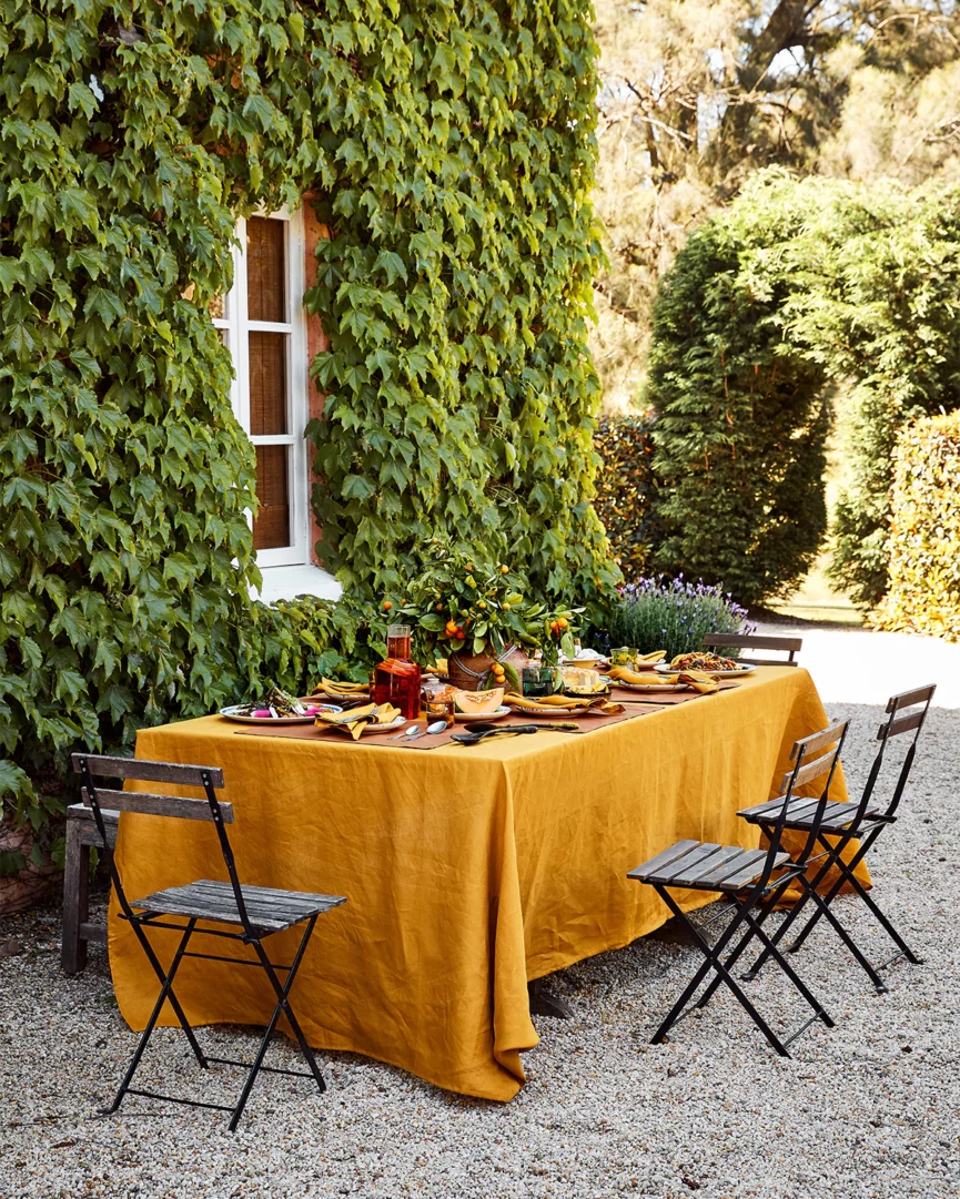 An outdoor dining table covered in a mustard tablecloth