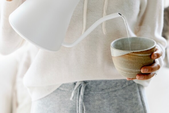 Pouring water from white electric tea kettle.