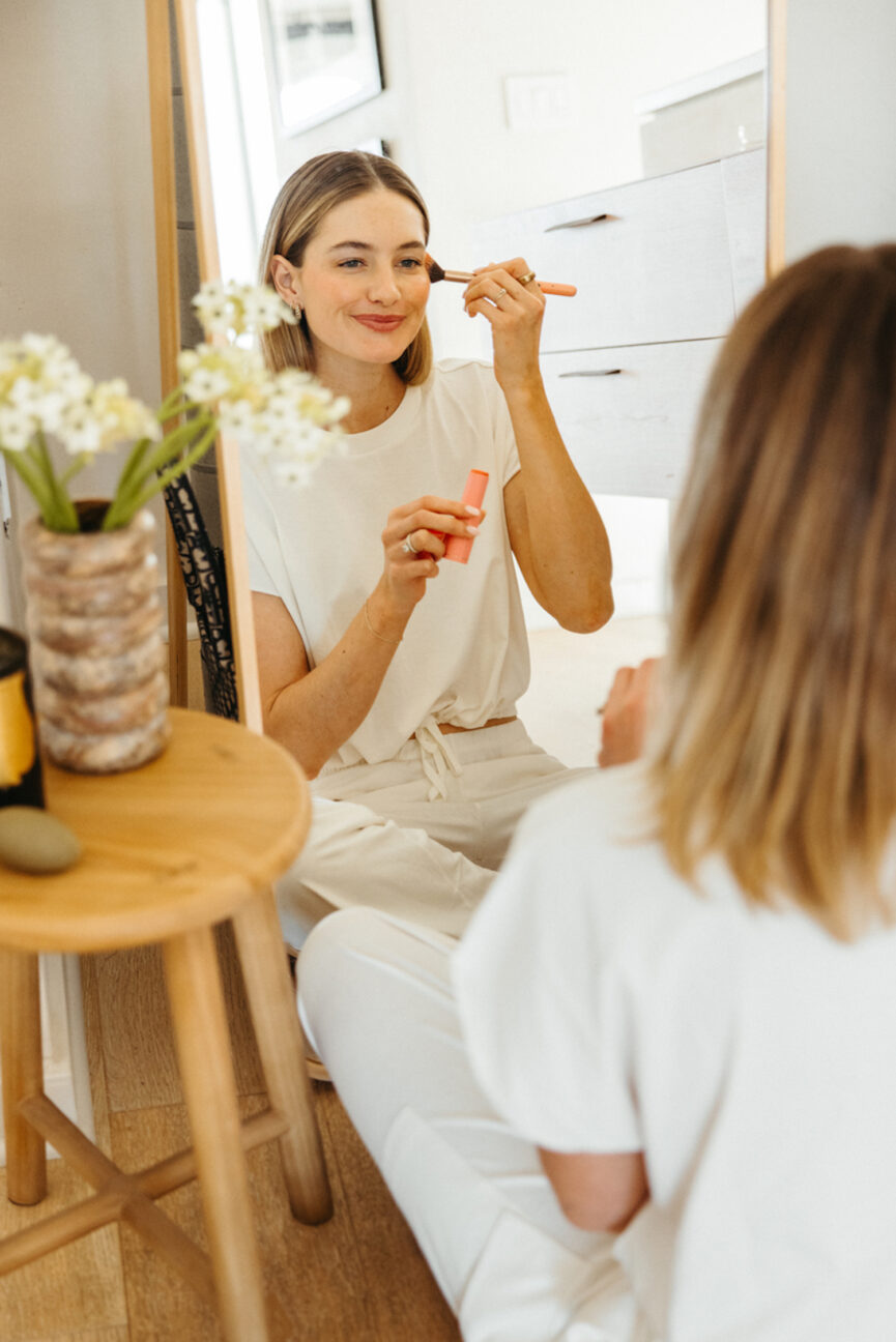 Woman applying makeup in mirror.
