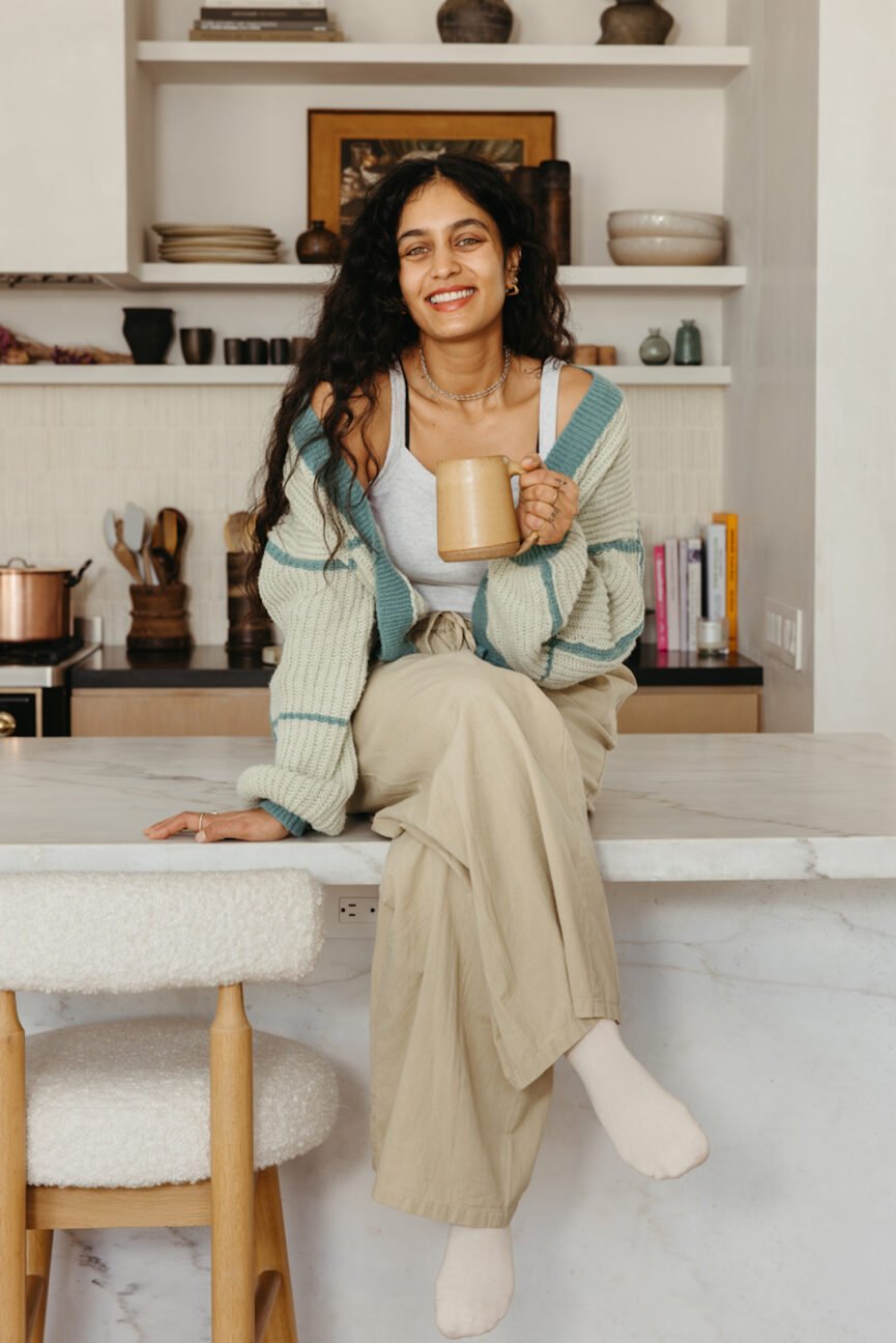 Woman drinking mug of tea sitting on kitchen counter.