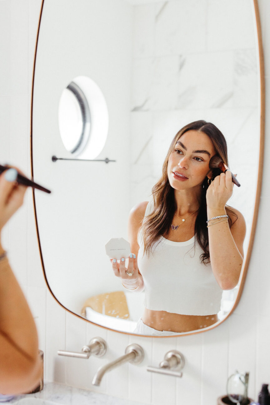 Woman applying makeup in mirror.