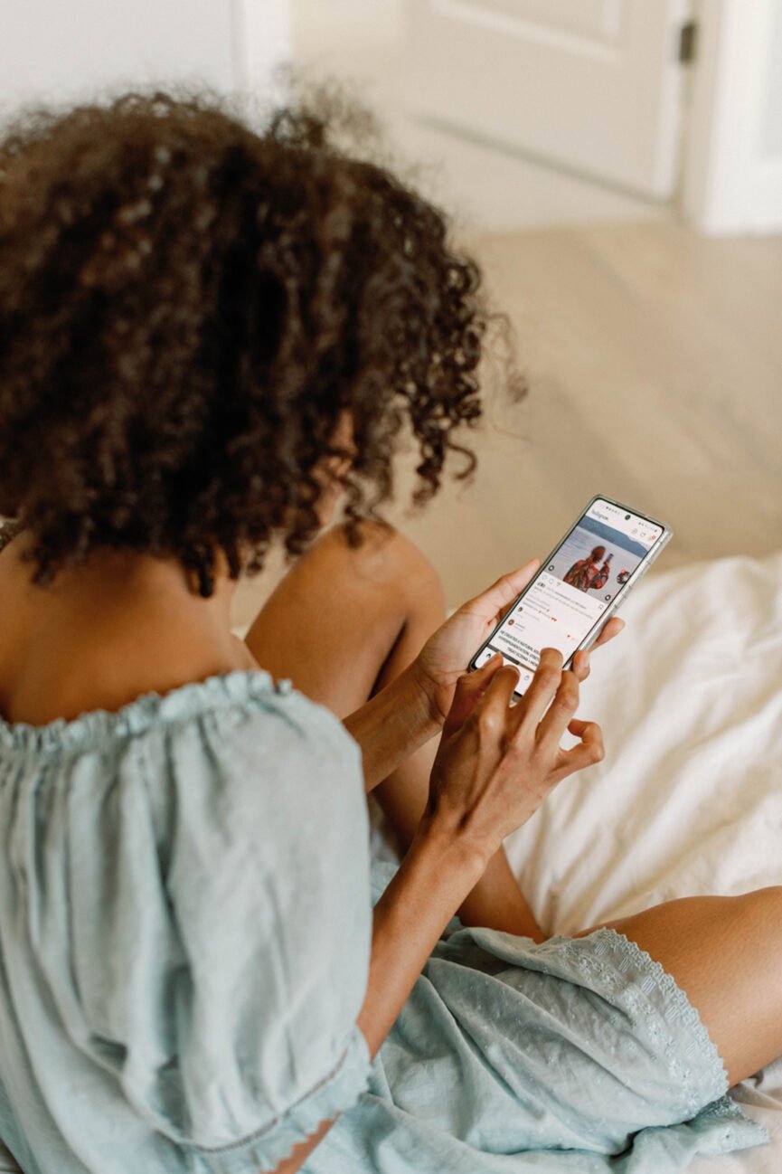 Mujer usando teléfono en la cama.